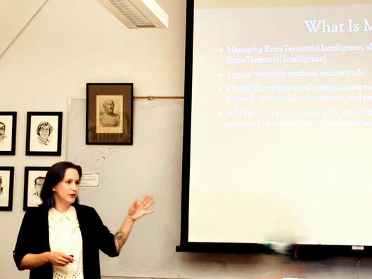 Dr. Haramia presenting with a raised arm gesturing to her slide on the screen to her side